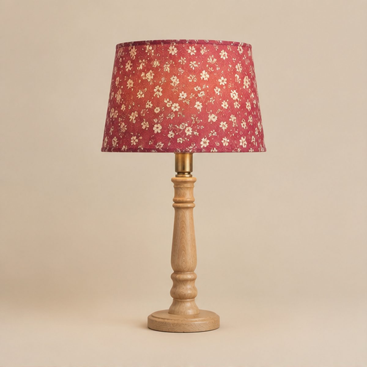 Home A table lamp with a pink floral shade lit above a turned light wood base, on a plain cream background