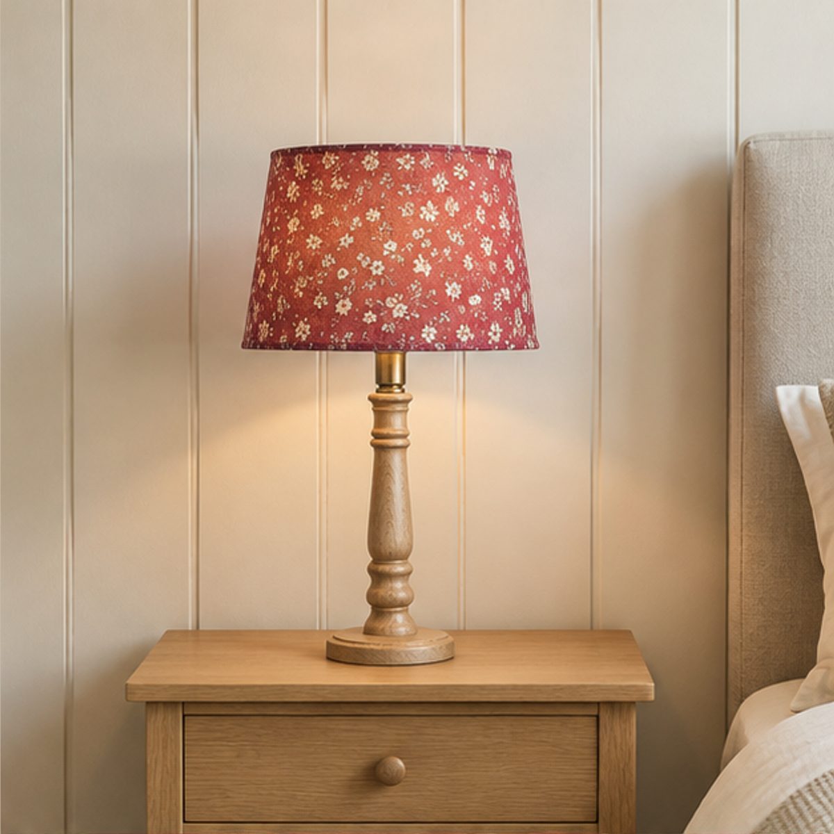 Sizing & Light Basics A table lamp with a pink floral shade lit on a wooden bedside table against a panelled wall