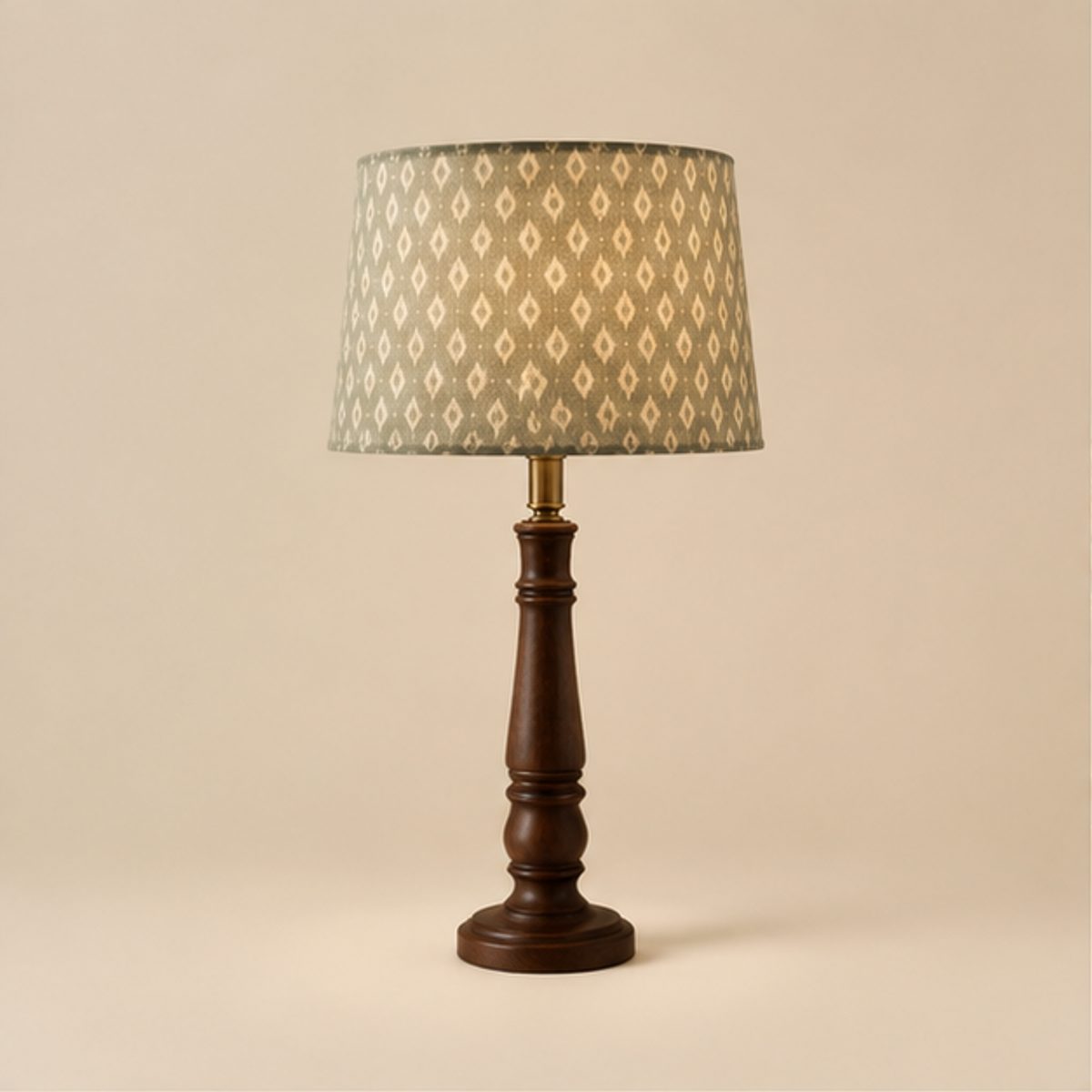 Home A table lamp with a green patterned shade lit above a turned dark wood base, on a plain cream background