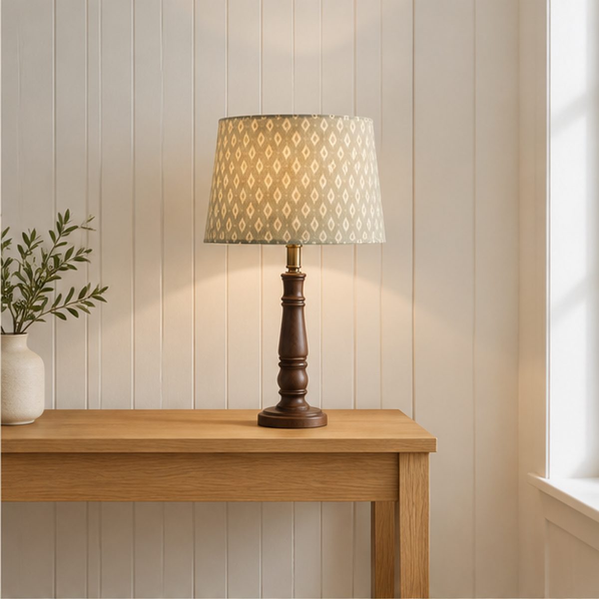 Home A table lamp with a green patterned shade lit on an oak console table against a panelled wall