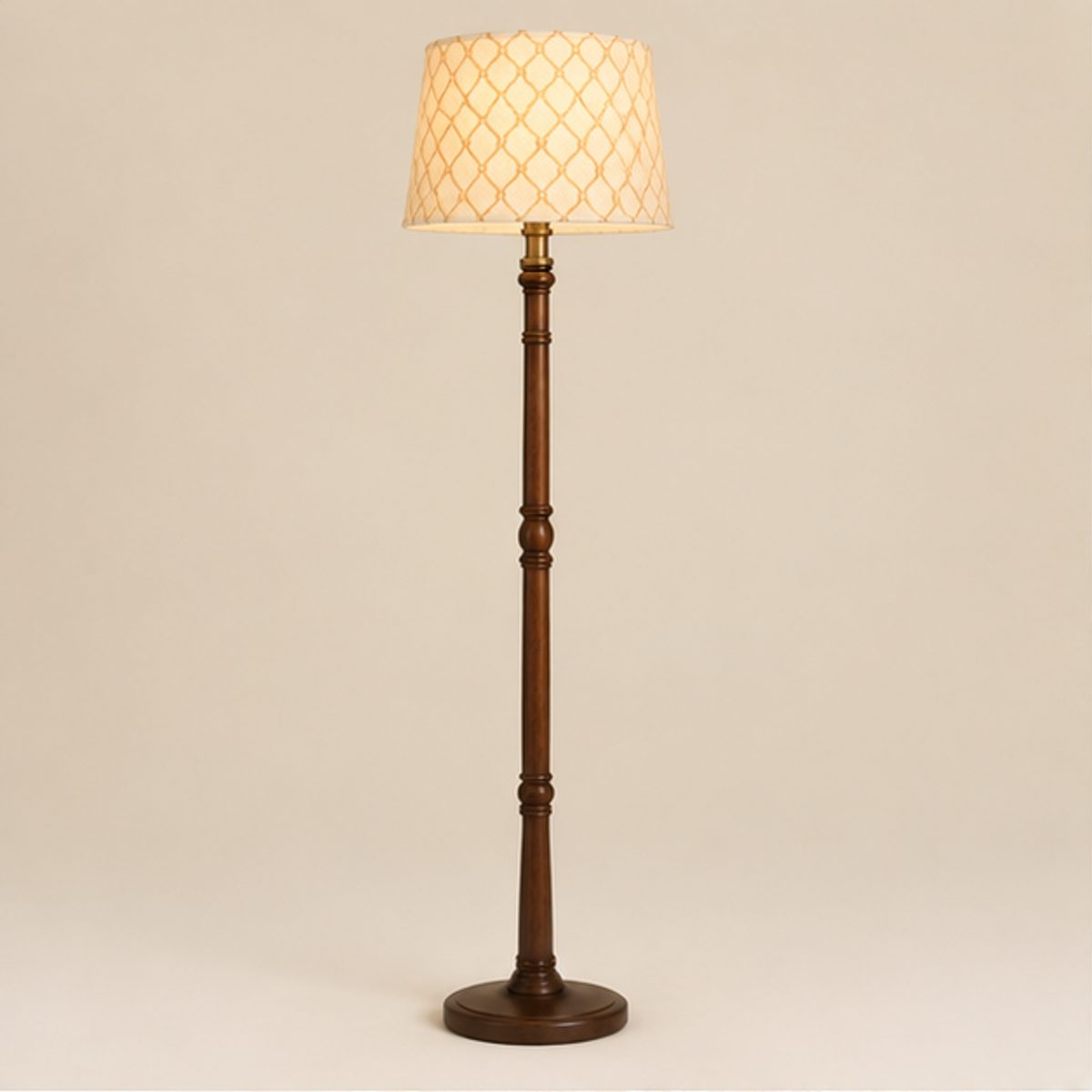 Home A floor lamp with a cream patterned shade lit on a turned dark wood column, on a plain cream background
