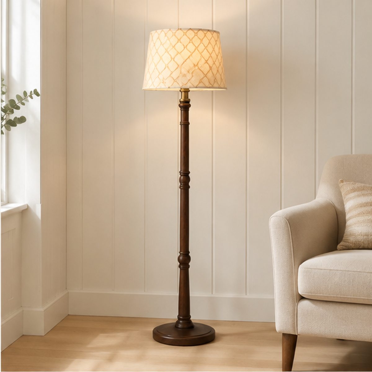 A floor lamp with a cream patterned shade lit beside an armchair in a room with a panelled wall
