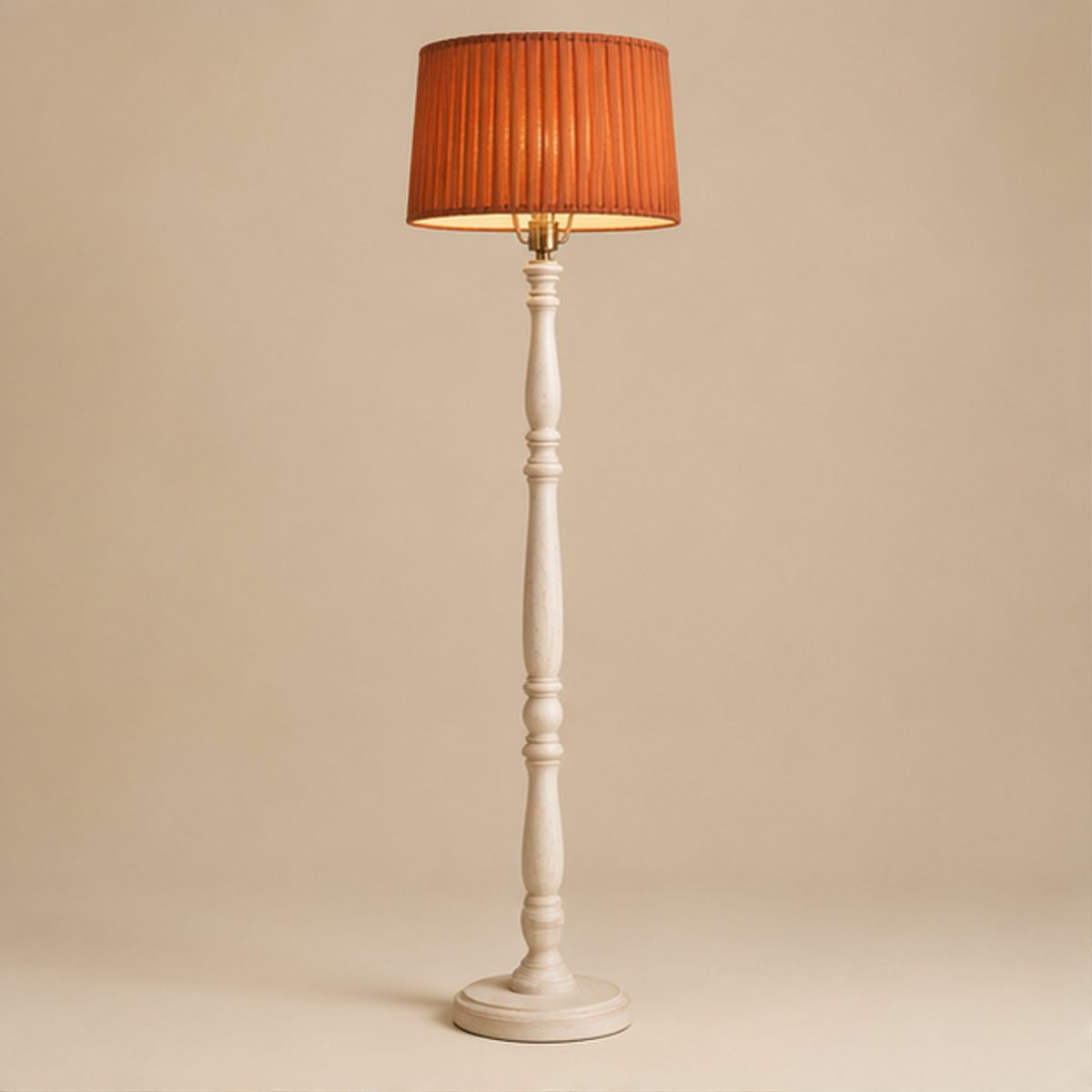 Home A floor lamp with a terracotta pleated shade lit on a turned whitewashed wood column, on a plain cream background