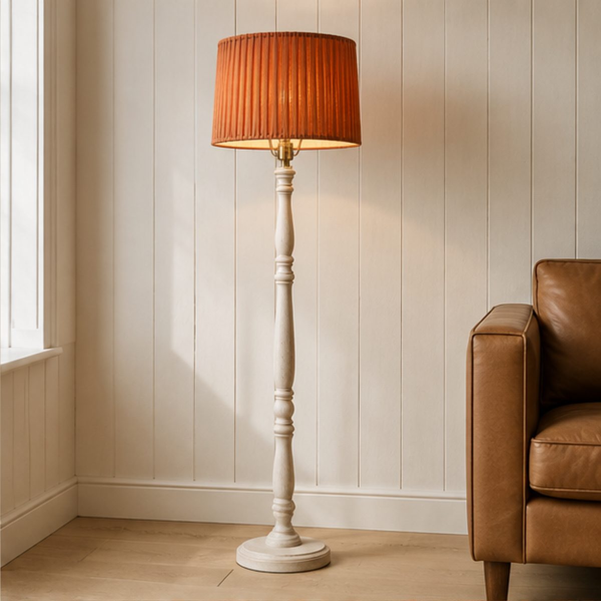 Home A floor lamp with a terracotta pleated shade lit beside a leather sofa in a room with a panelled wall